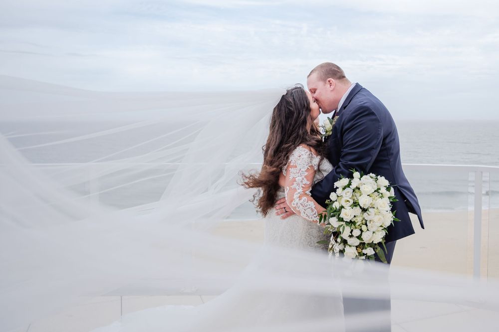 Windy Day Wedding - Flowing Veil Photo - Bride and Groom Kissing by Beach and Ocean - Lynn Monaco Photography