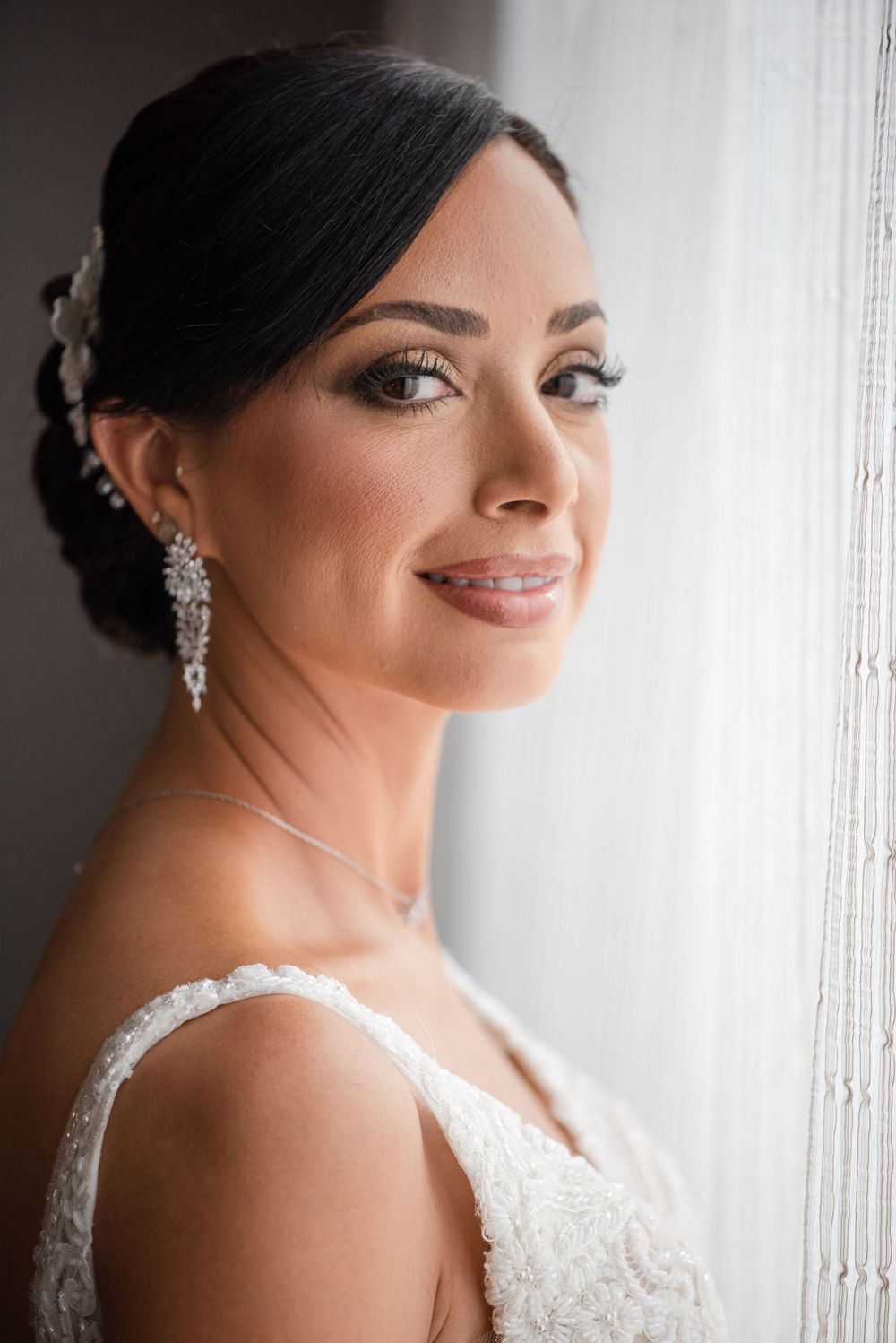 Elegant bridal portraits showcasing sparkling earrings and lace details against a light window background.