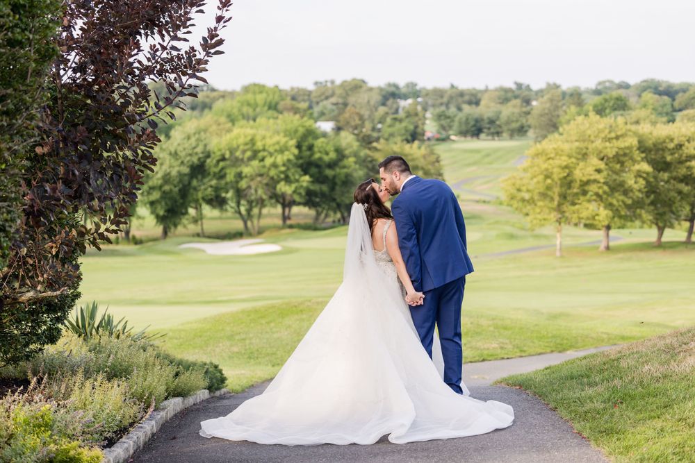 A bride and groom walk hand in hand across a scenic golf course.