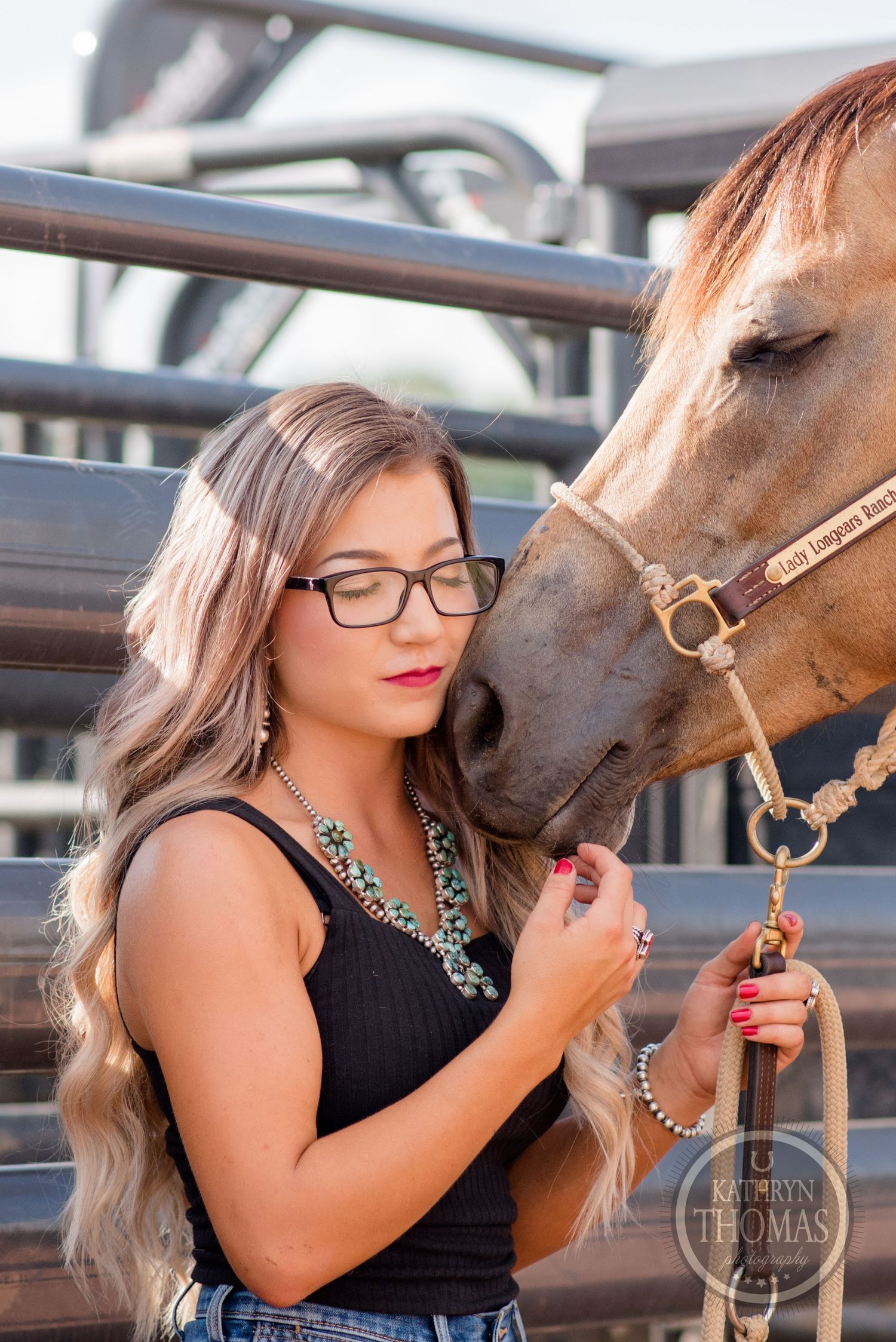 A close-up photo shows tender moment between a brown horse and its handler near metal stables.