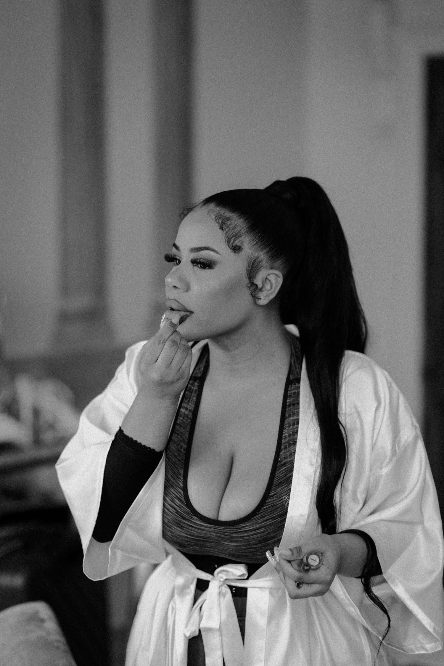 Black and white portrait of someone in a silk robe getting ready with glamorous makeup.