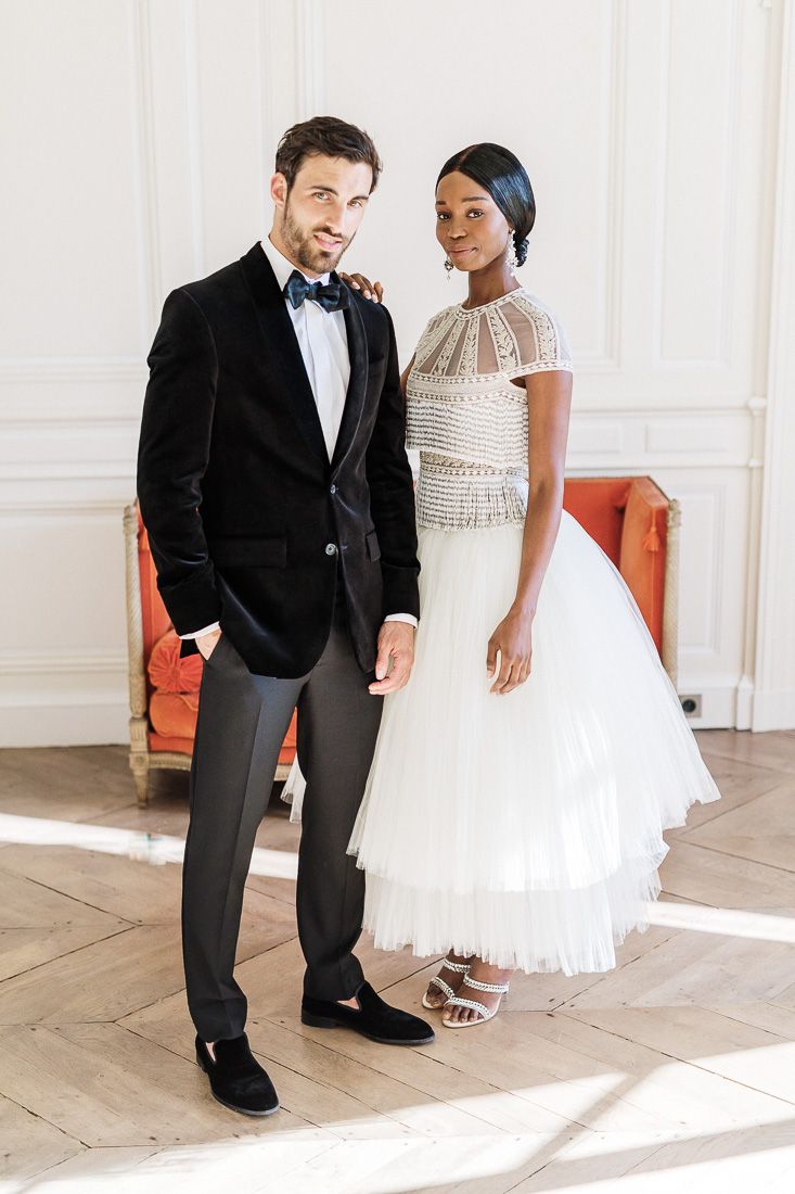 Formal couple posing in elegant attire against white wall interior.