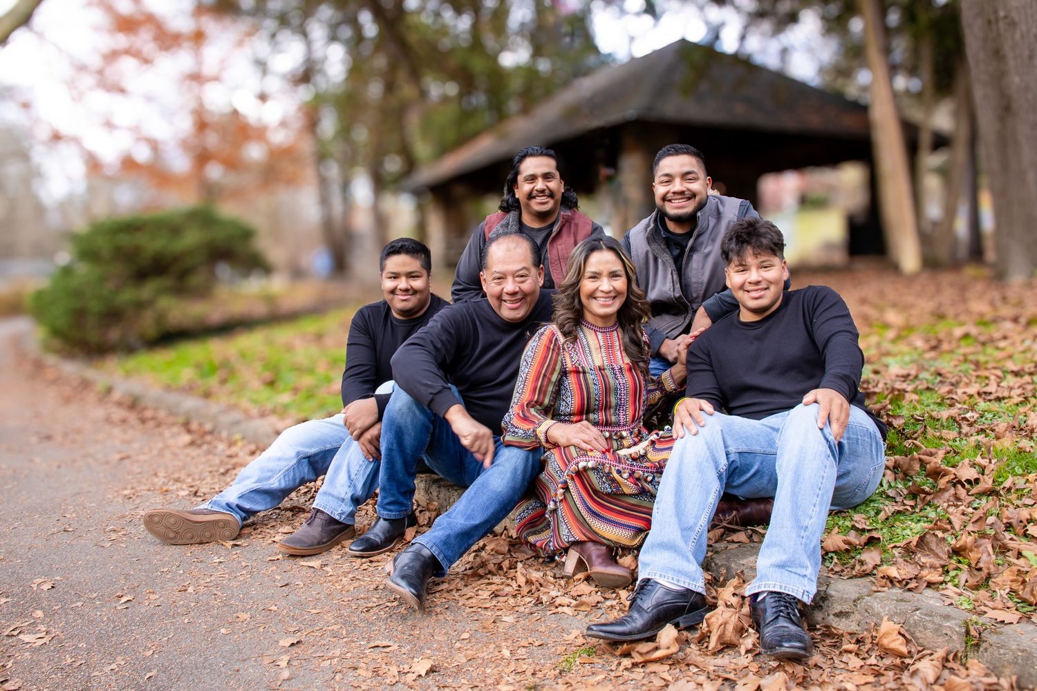 Happy Latino family of six smiling together outdoors on a fall day surrounded by autumn leaves in a park.