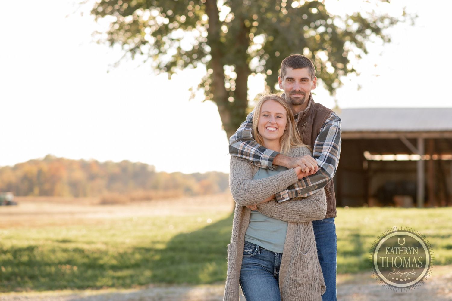A couple embracing in front of a barn during golden hour.