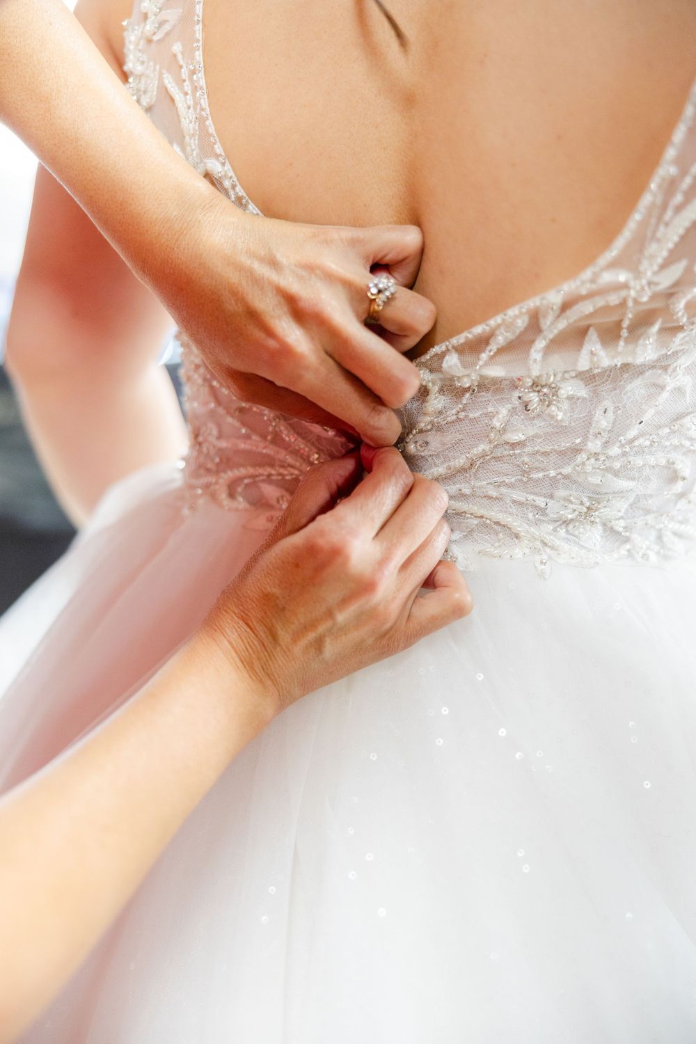 Close-up of hands fastening delicate buttons on a white lace wedding dress.