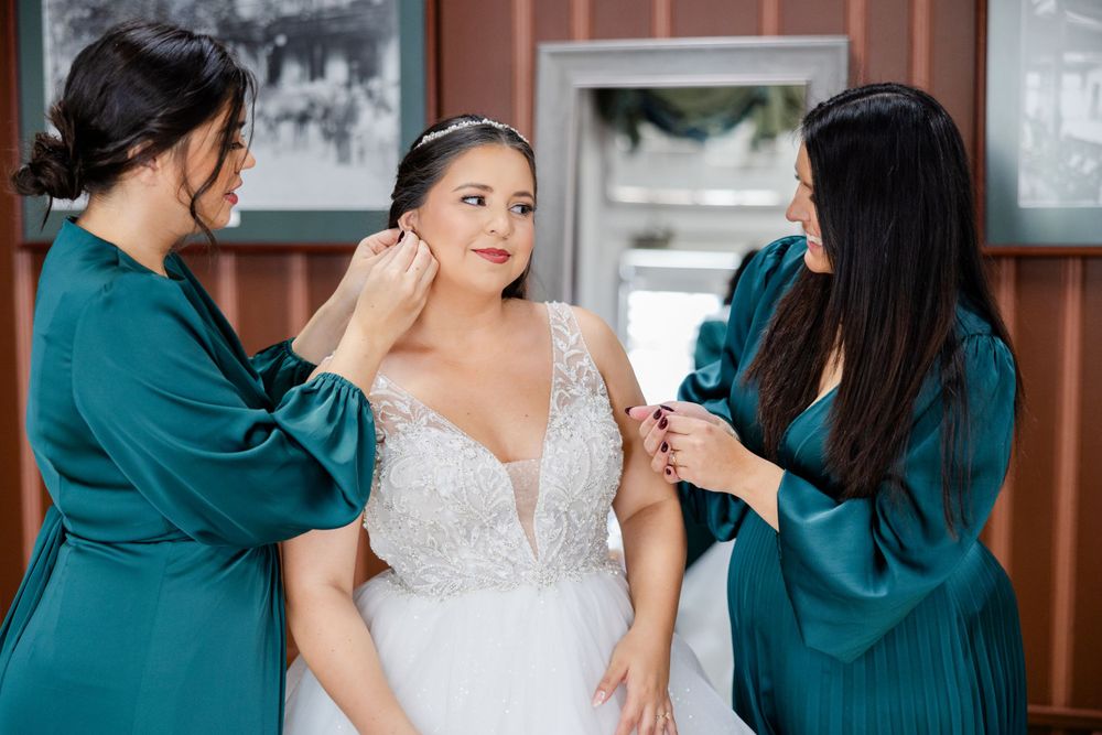 Bridesmaids in teal dresses help adjust the wedding dress during pre-ceremony preparations.