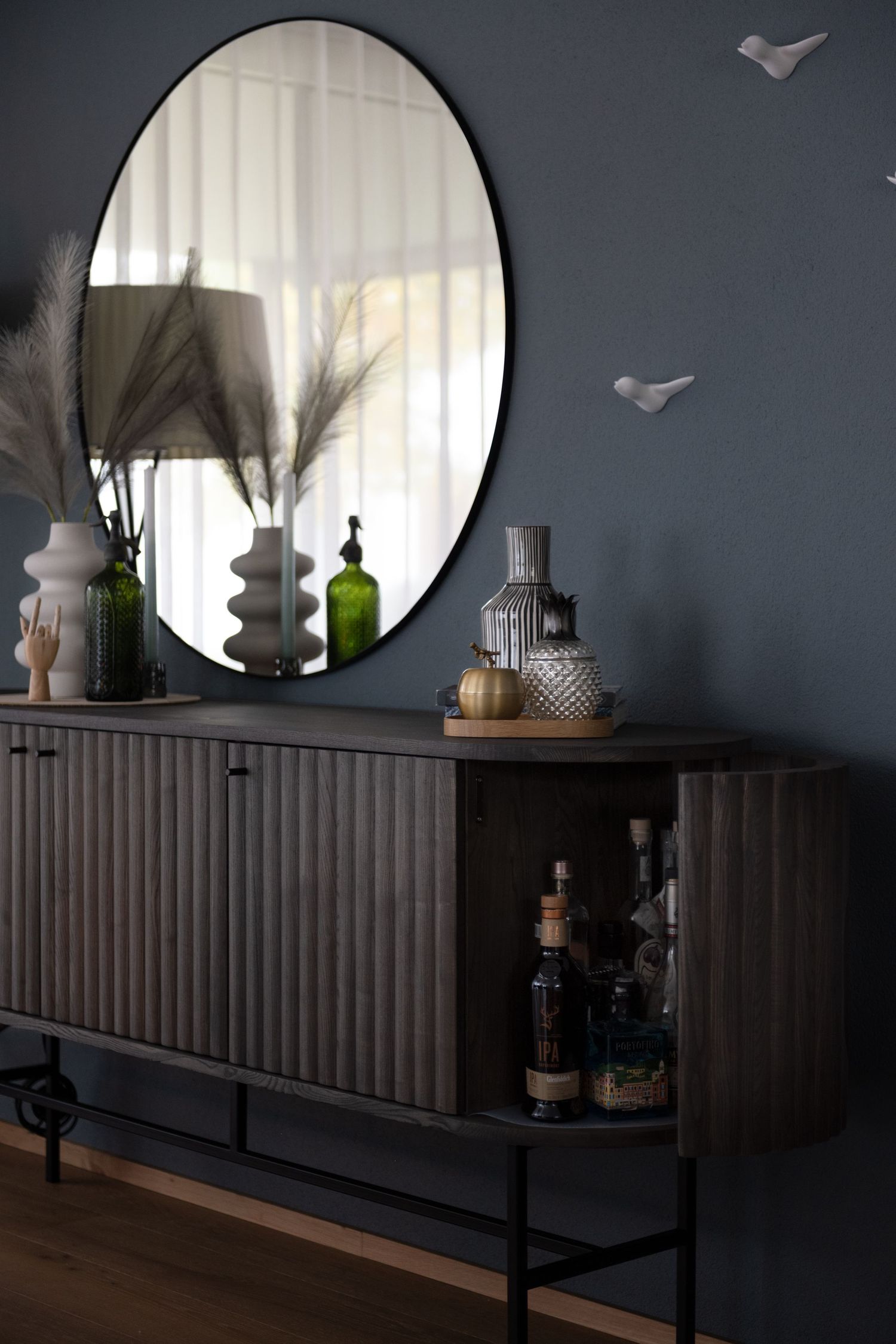 A round mirror above a cupboard with a drinks section