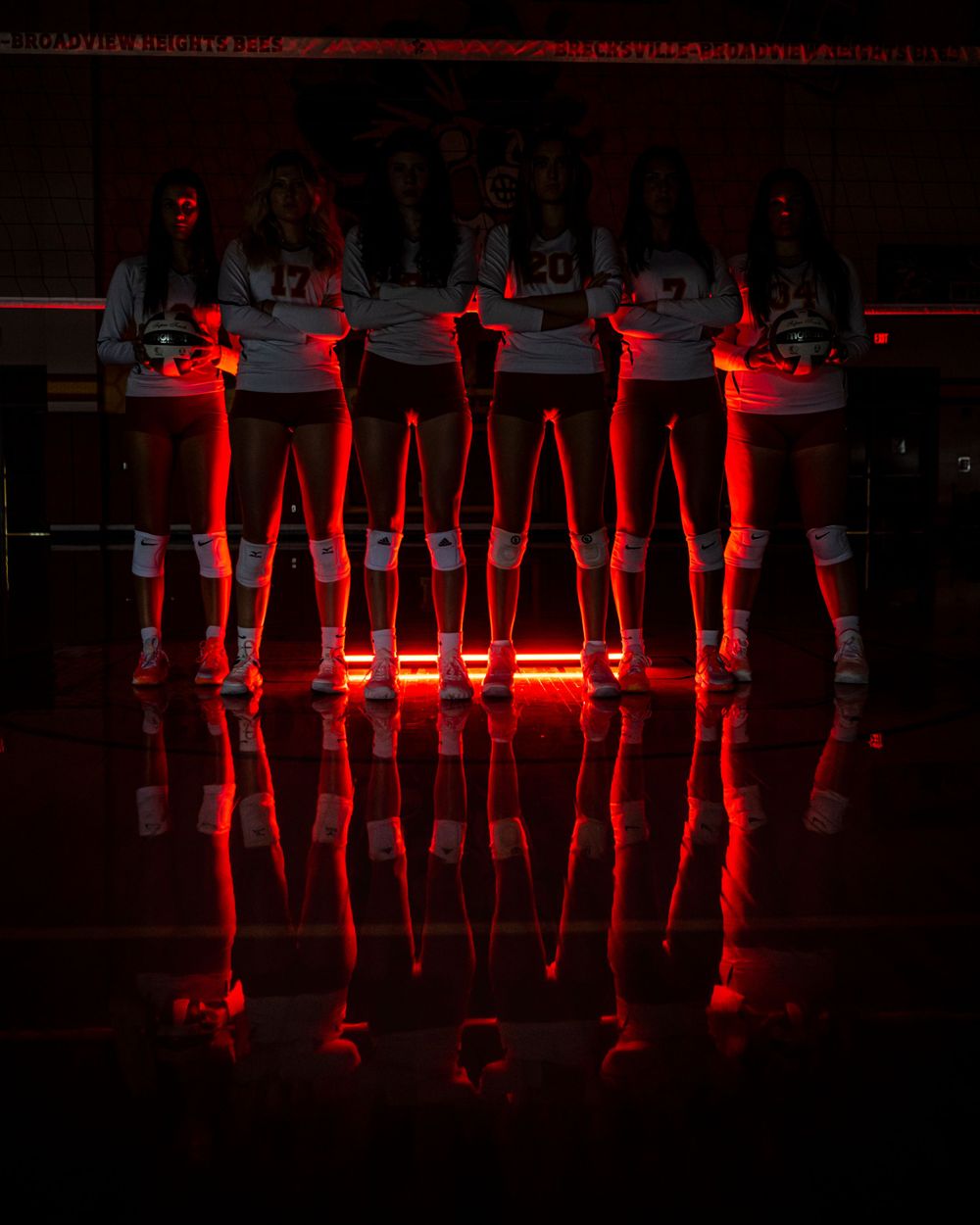 Silhouetted figures standing in dramatic red lighting with reflective floor effect.  Brecksville Lady Bees, Ohio