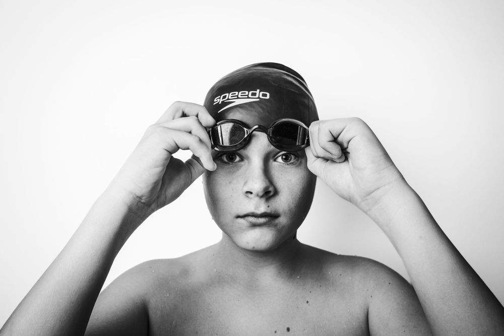 Swimmer adjusting goggles and swim cap in black and white portrait style.