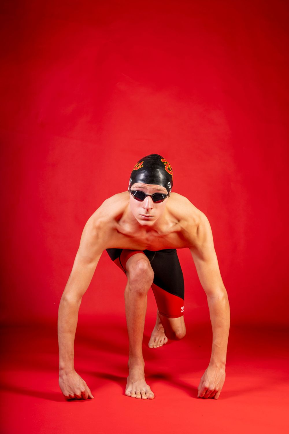 Competitive swimmer in starting position against vibrant red background.