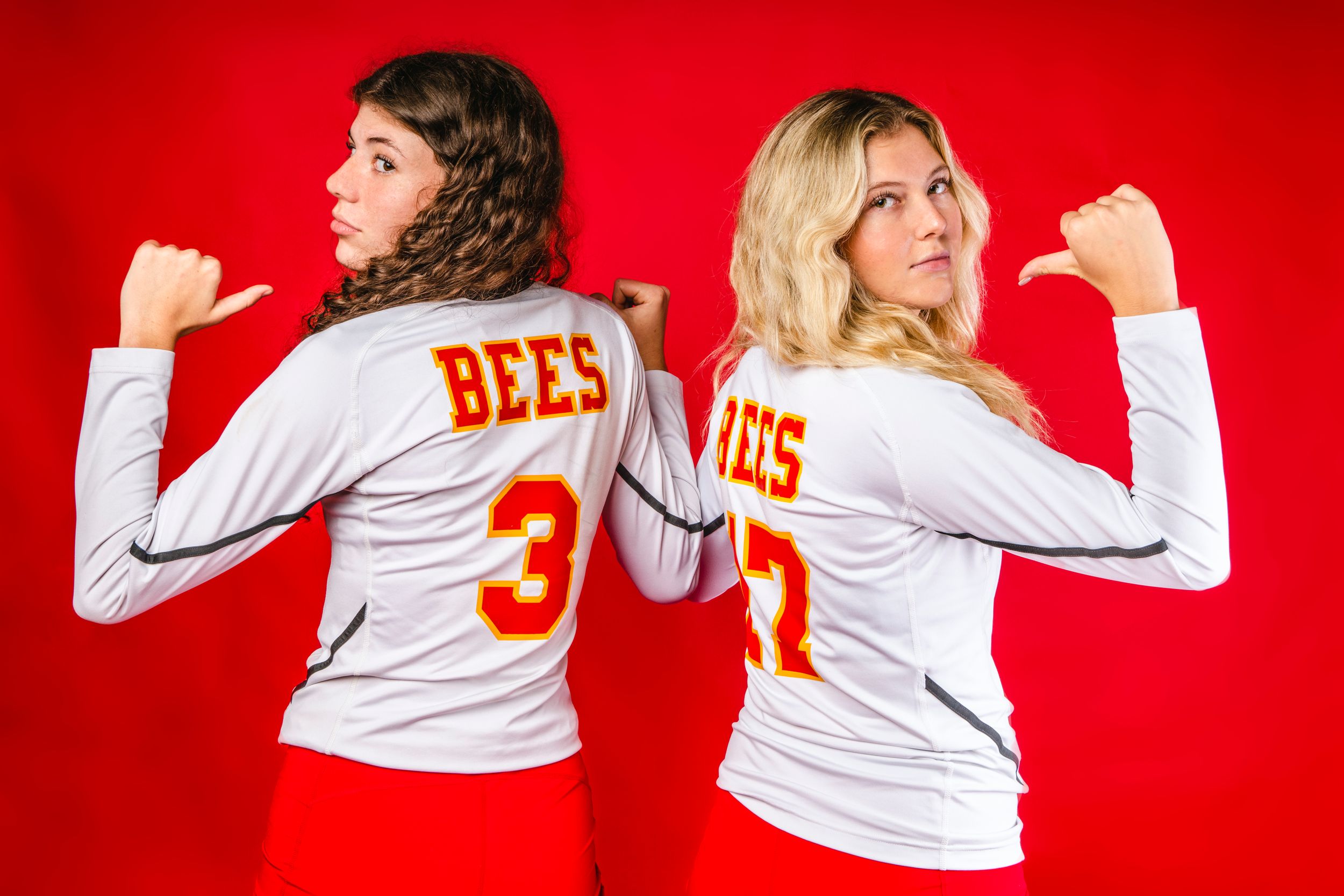 Two friends in white jerseys with 'BEES' text pose back-to-back against red background.  Brecksville Lady Bees, Ohio