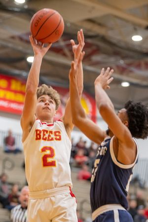 Basketball player in white jersey takes a jump shot while being defended during game action.