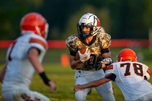 Football player in metallic uniform breaking through defenders during sunset game.