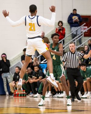 Basketball players jumping during an intense game with referee and spectators in background.