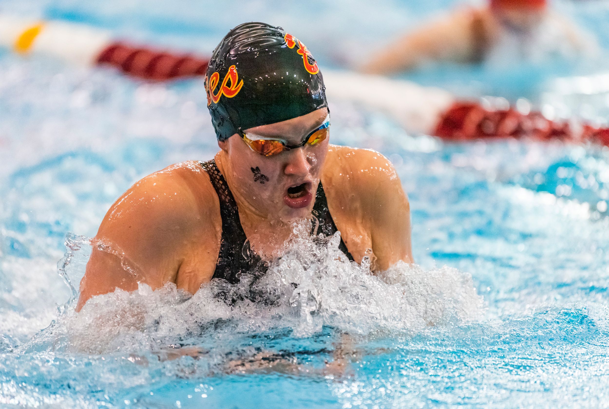 A competitive swimmer in black cap performs breaststroke during a race in a pool.
