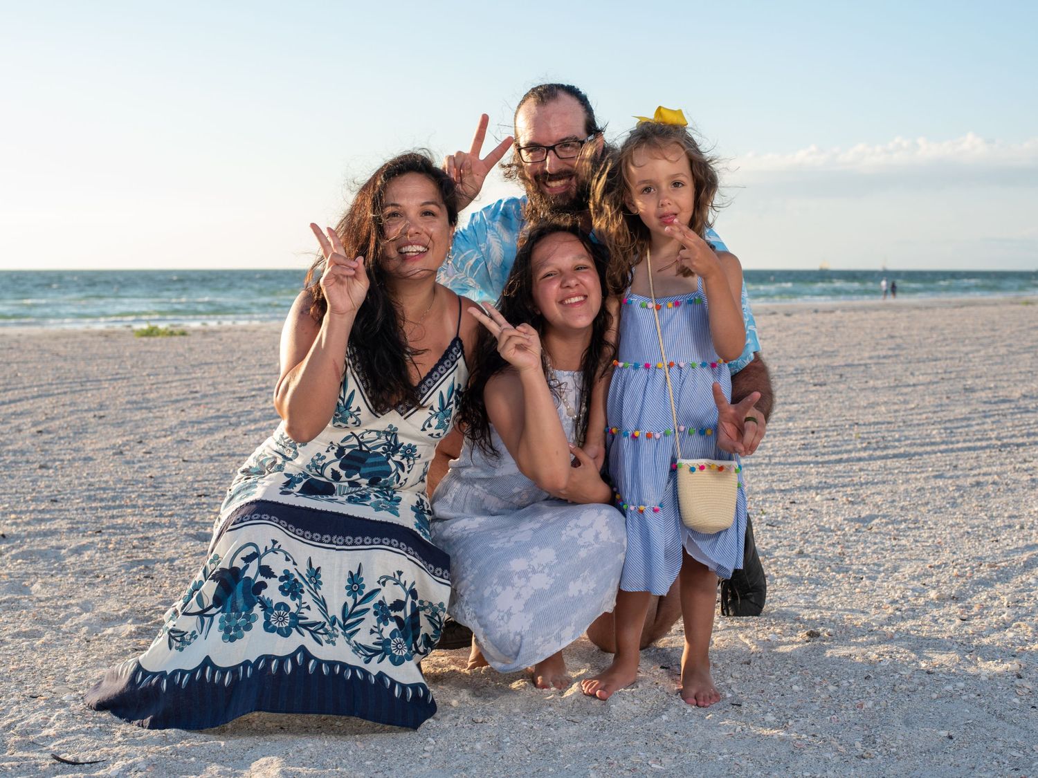 Happy family posing together on sunny beach with peace signs.