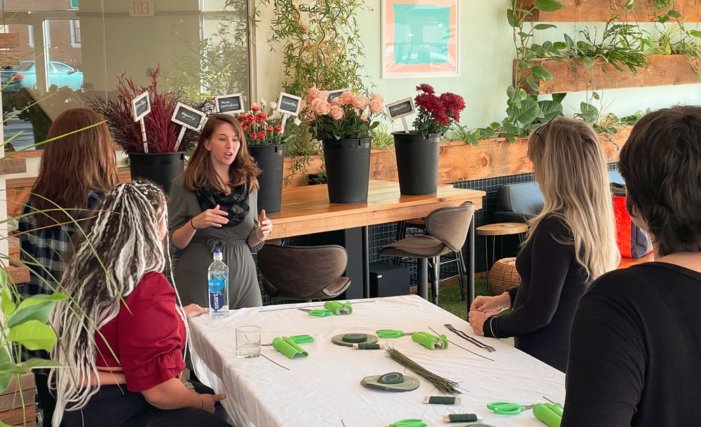 Workshop participants gathered around table with flower arrangements and supplies.