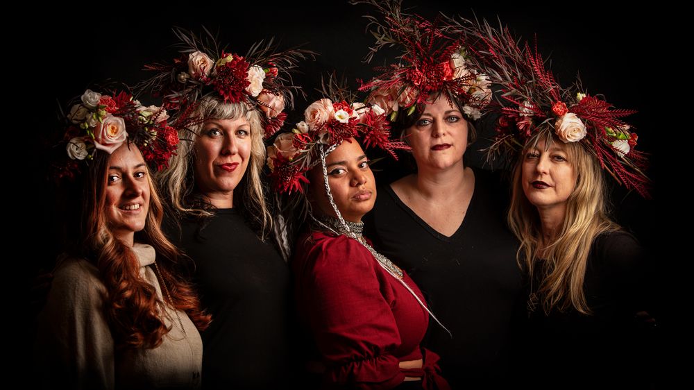 Group portrait with dramatic floral headpieces against black background.