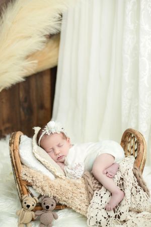 Sleeping newborn rests peacefully on lace blanket with small knitted teddy bear toys.
