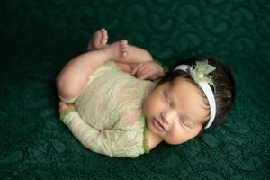 Sleeping newborn in delicate lace outfit on dark green textured backdrop.