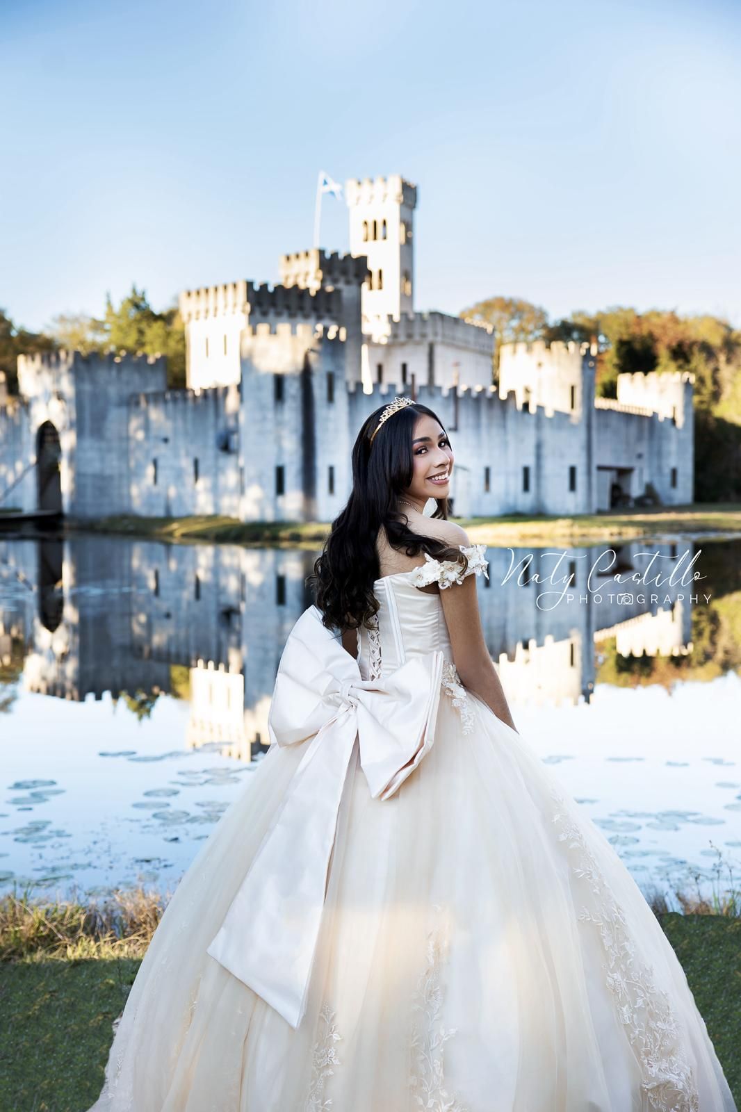 Romantic bridal portrait in white gown with castle and reflective lake in background.