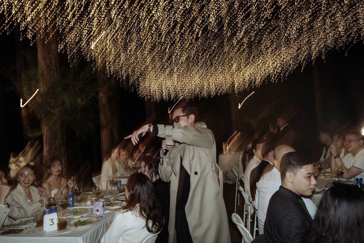 Wedding guest performer entertaining crowd under golden fairy light canopy at outdoor reception.