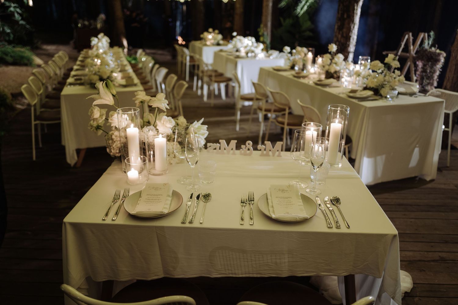 Elegant outdoor wedding reception table setting with candles and white linens at night.