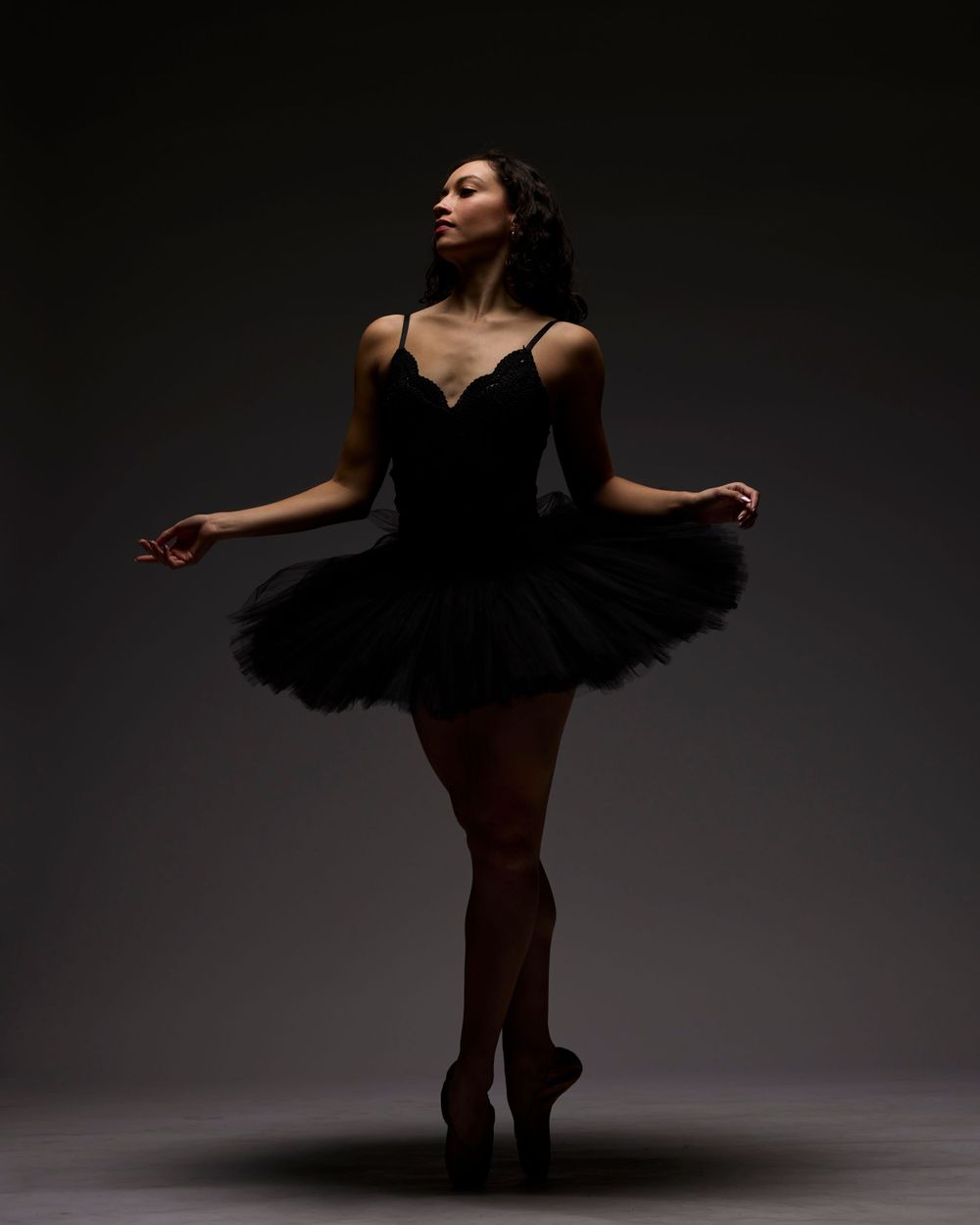 Ballet dancer in black tutu performing graceful pose in dramatic lighting.