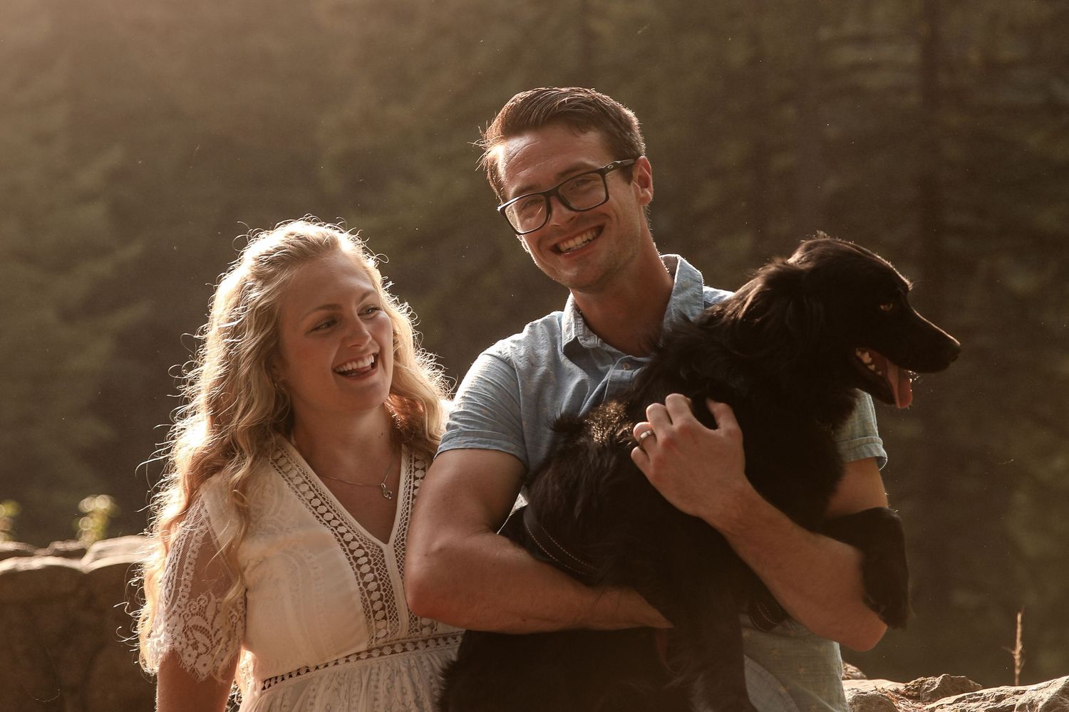 Couple with black dog sharing tender moment during golden hour in nature.