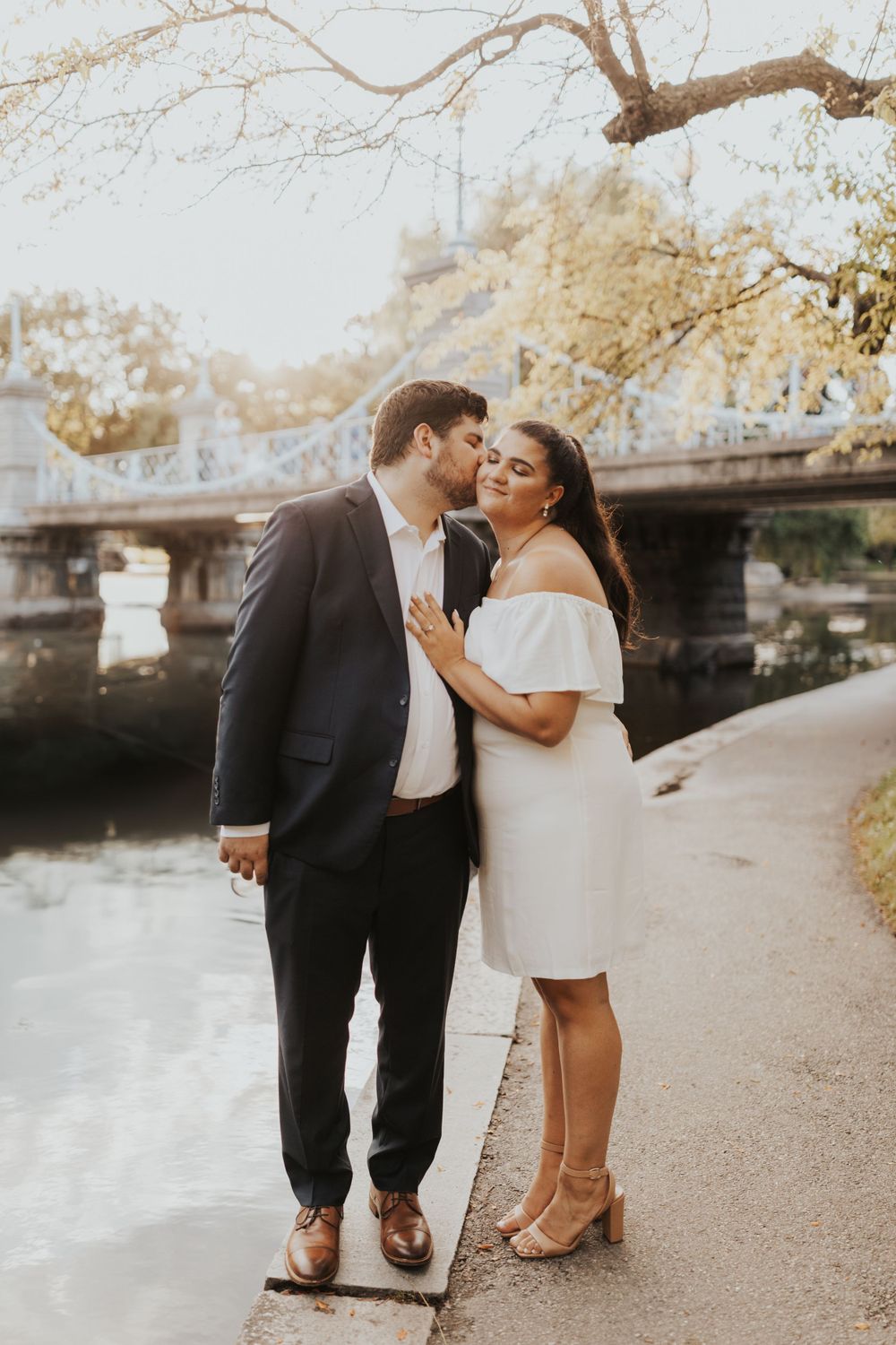 A couple shares a romantic moment along a riverside path during golden hour.