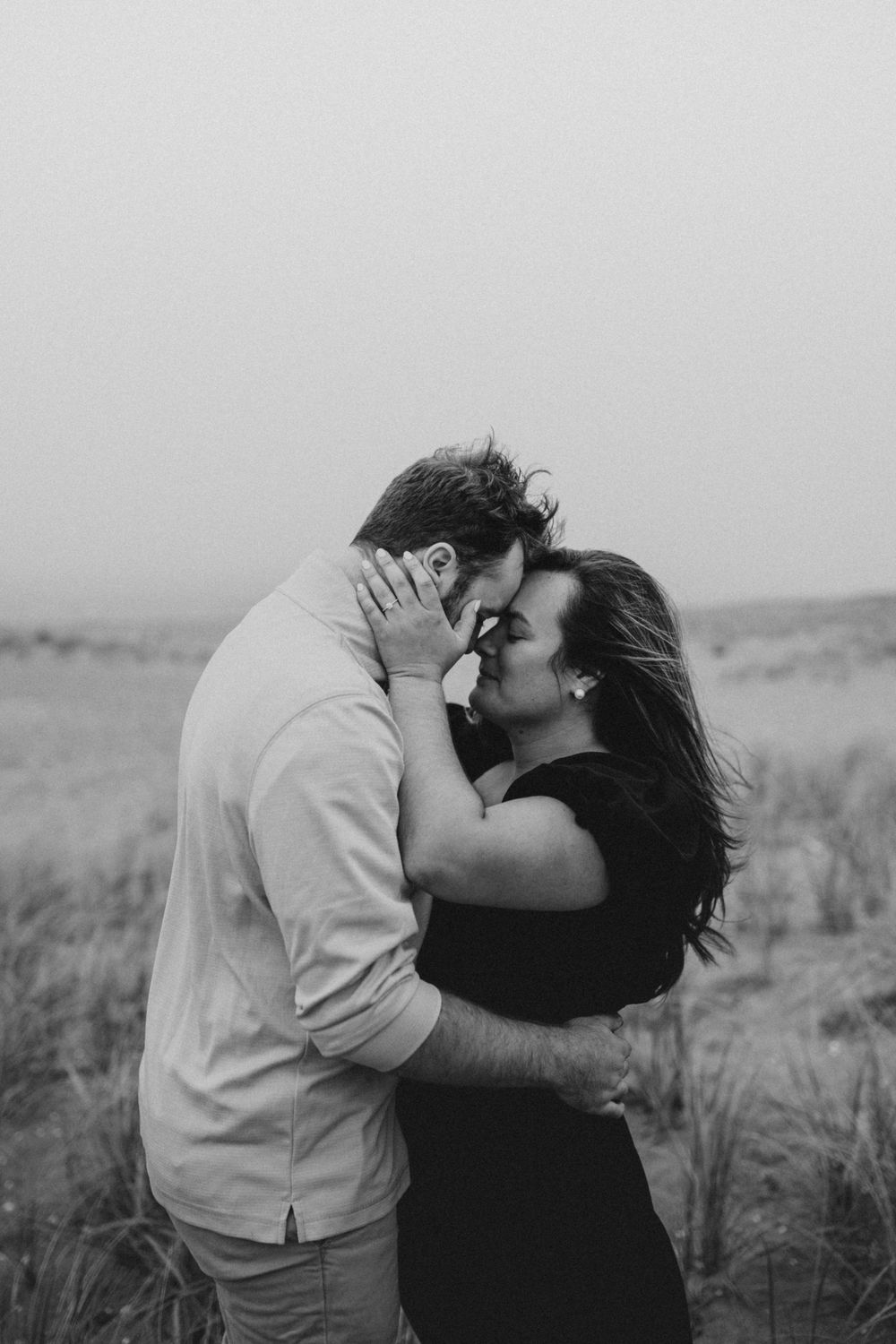 Intimate black and white portrait of couple embracing in windswept field.