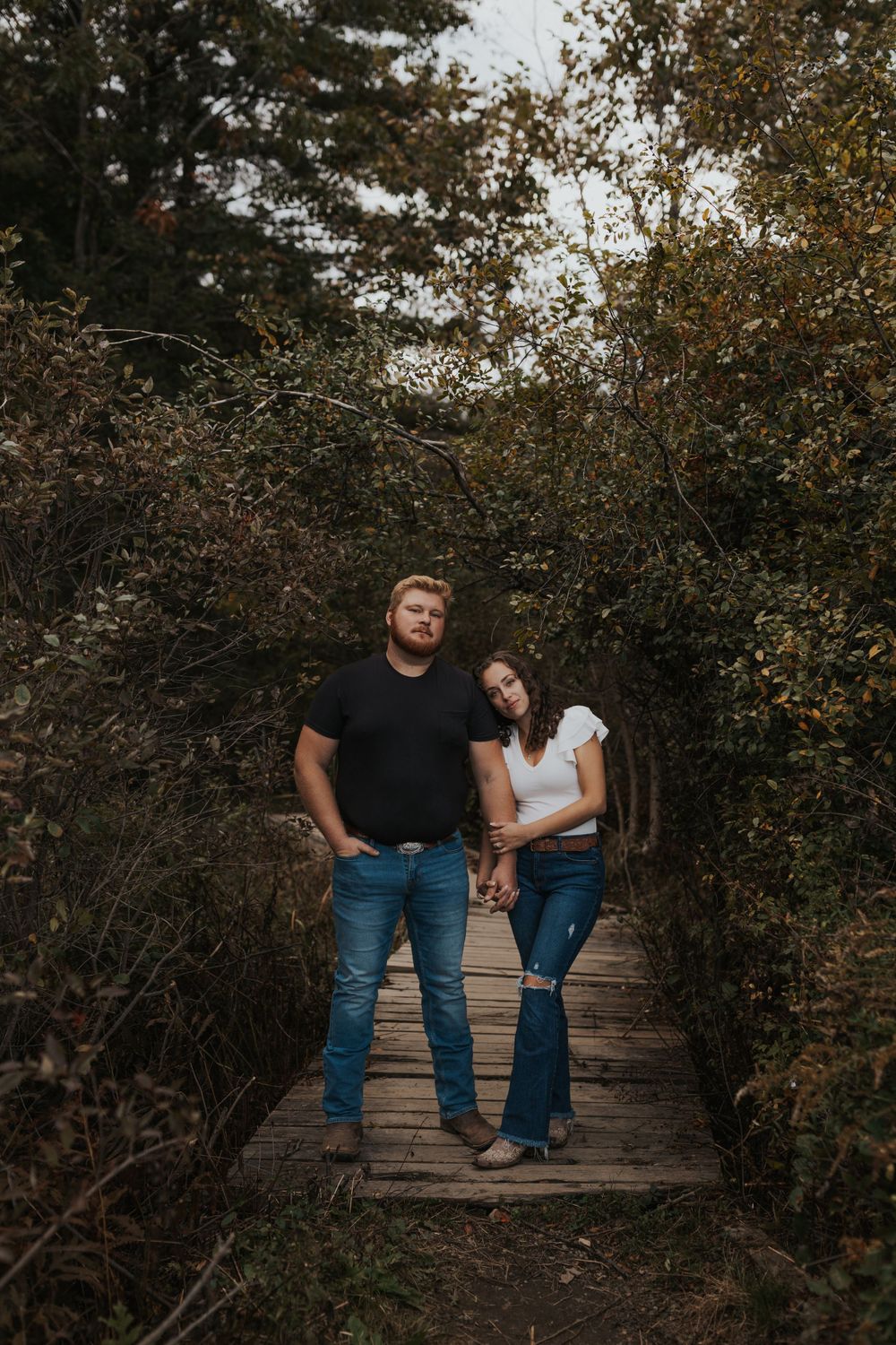 A couple stands together on a wooden boardwalk surrounded by fall foliage.