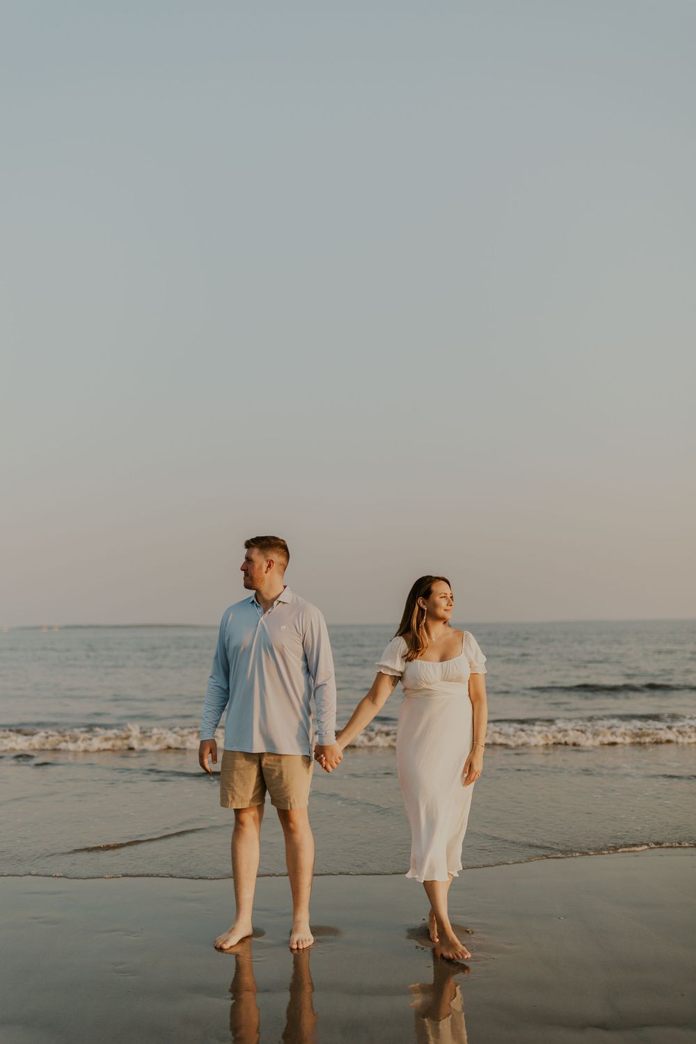 A couple walks hand in hand along a beach at sunset with gentle waves in the background.