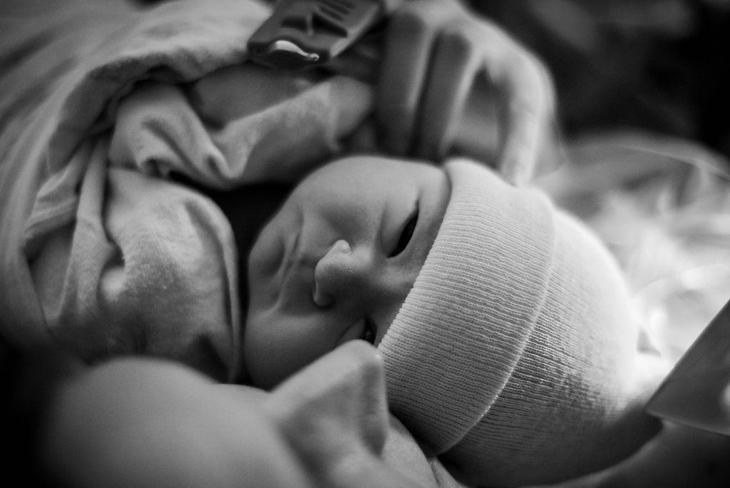Close-up black and white image of a newborn baby with hospital cap.