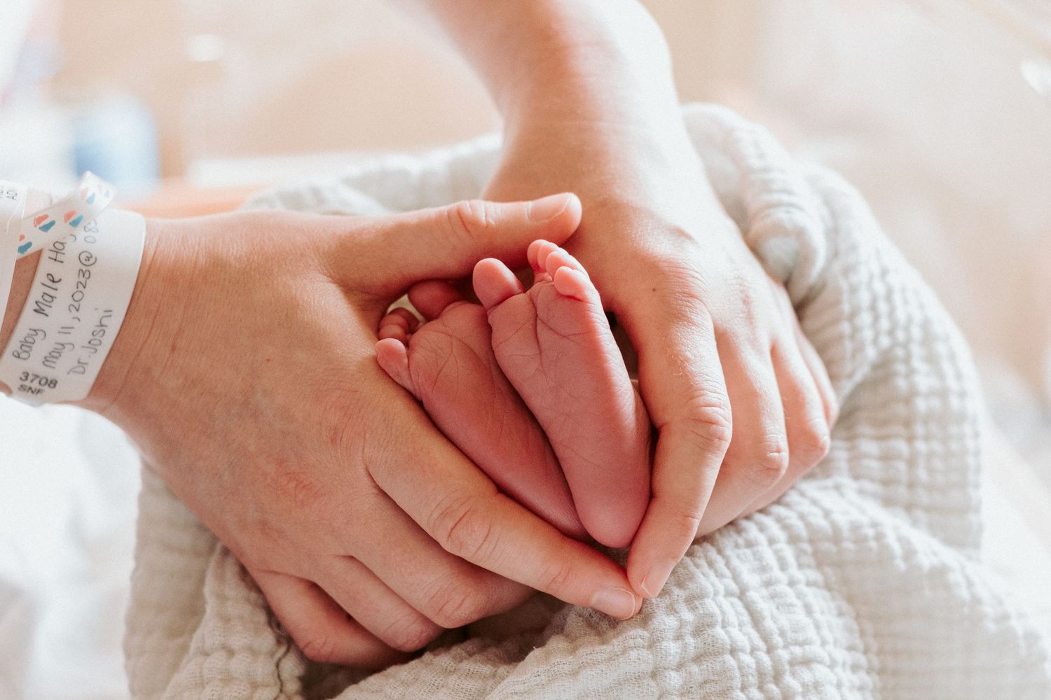 Tiny newborn baby feet gently held in adult hands with white blanket background.