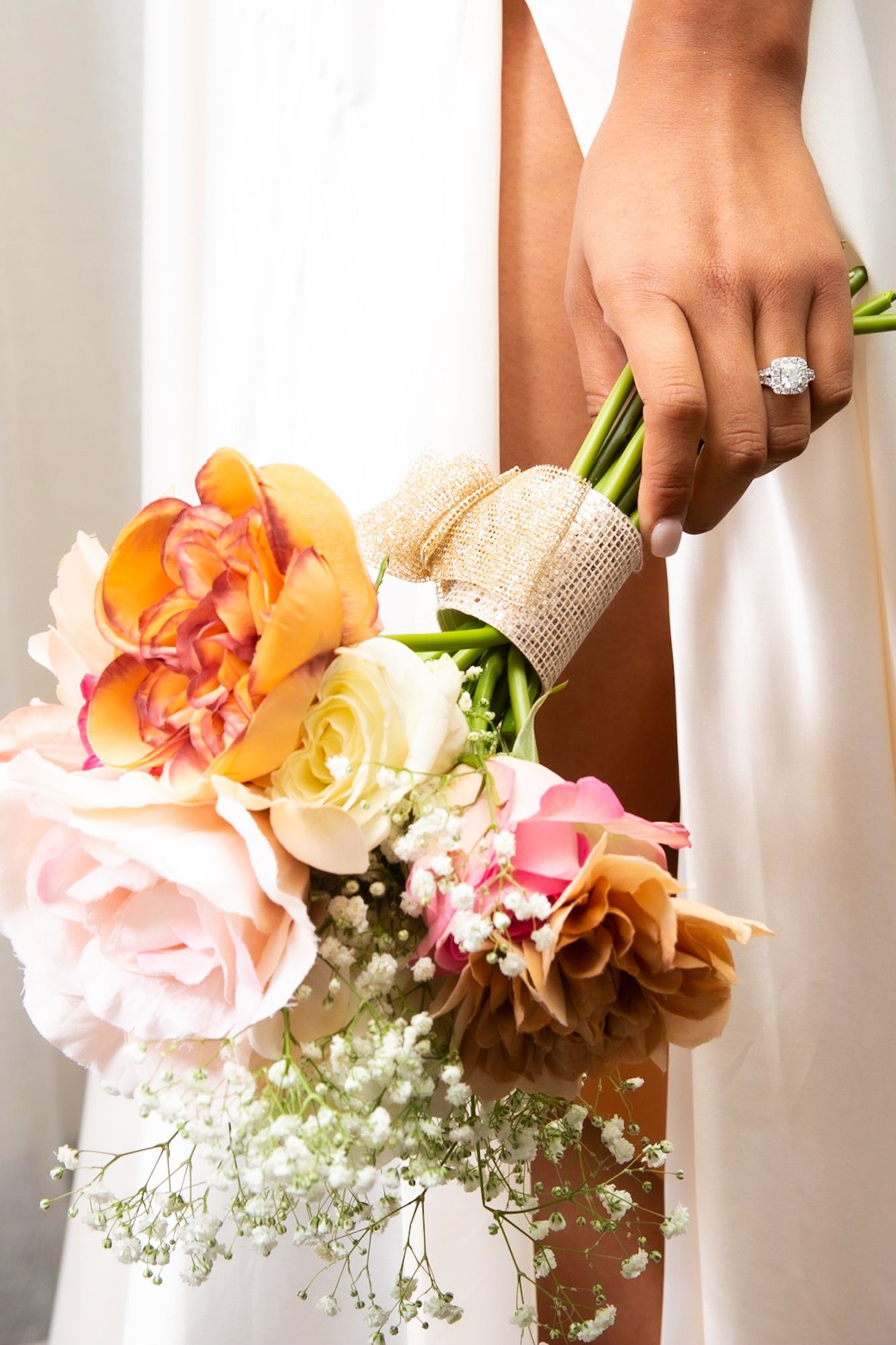 Bride holds a colorful wedding bouquet of roses and flowers while wearing a diamond engagement ring.