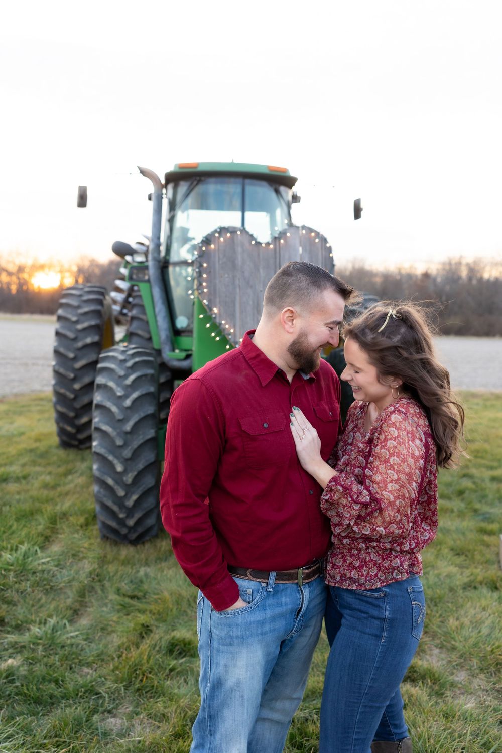 A couple laughs together during their engagement photos with a tractor backdrop.