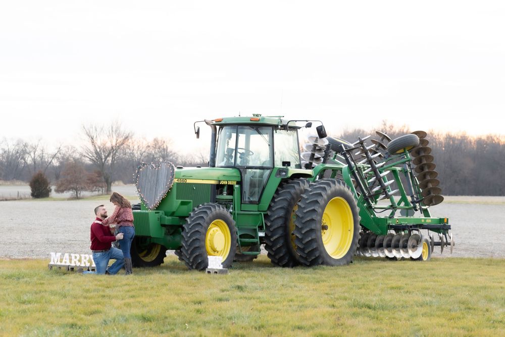 Green John Deere tractor with tillage equipment attached parked in open field.