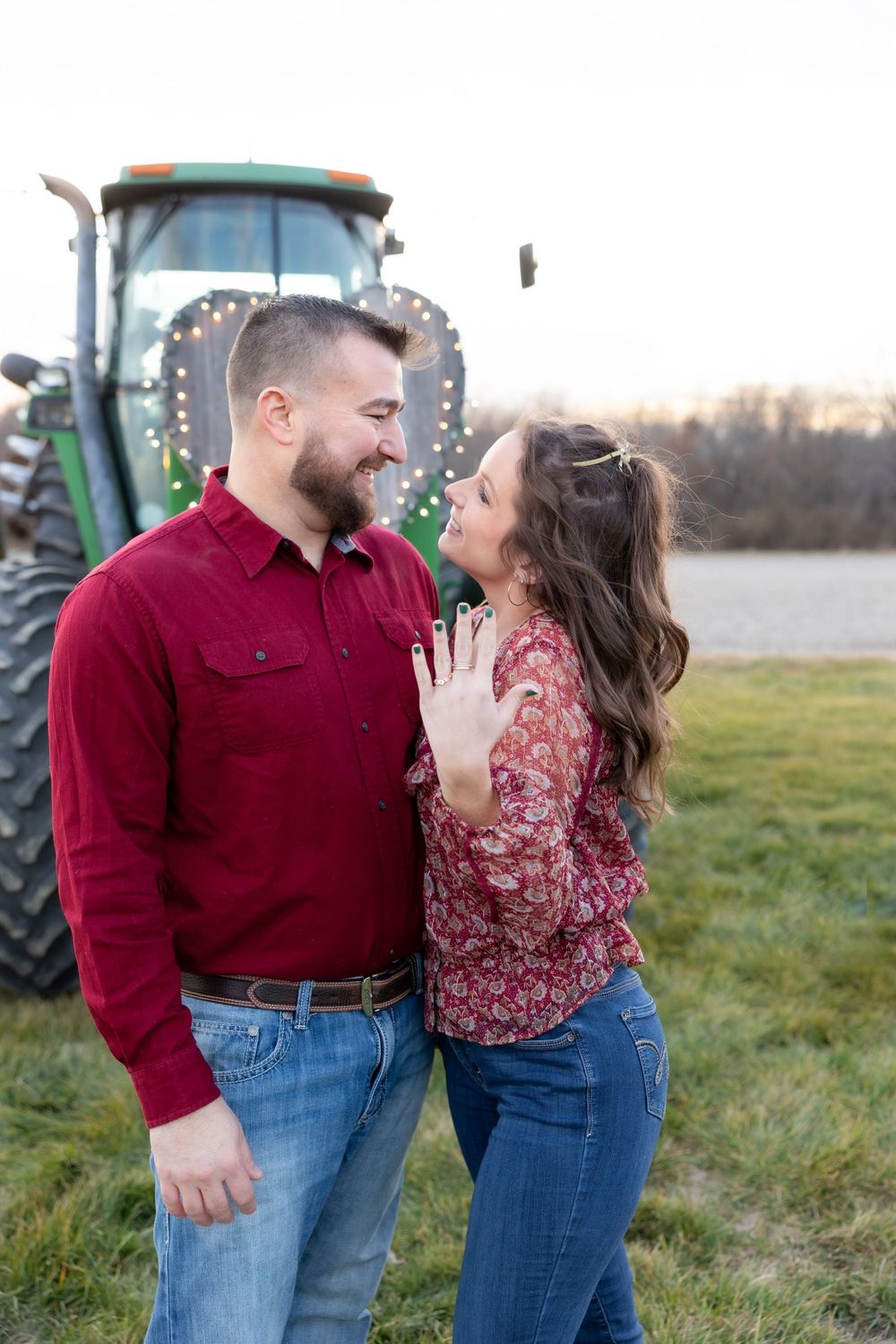 A couple shares a joyful moment in front of a decorated tractor during their engagement.