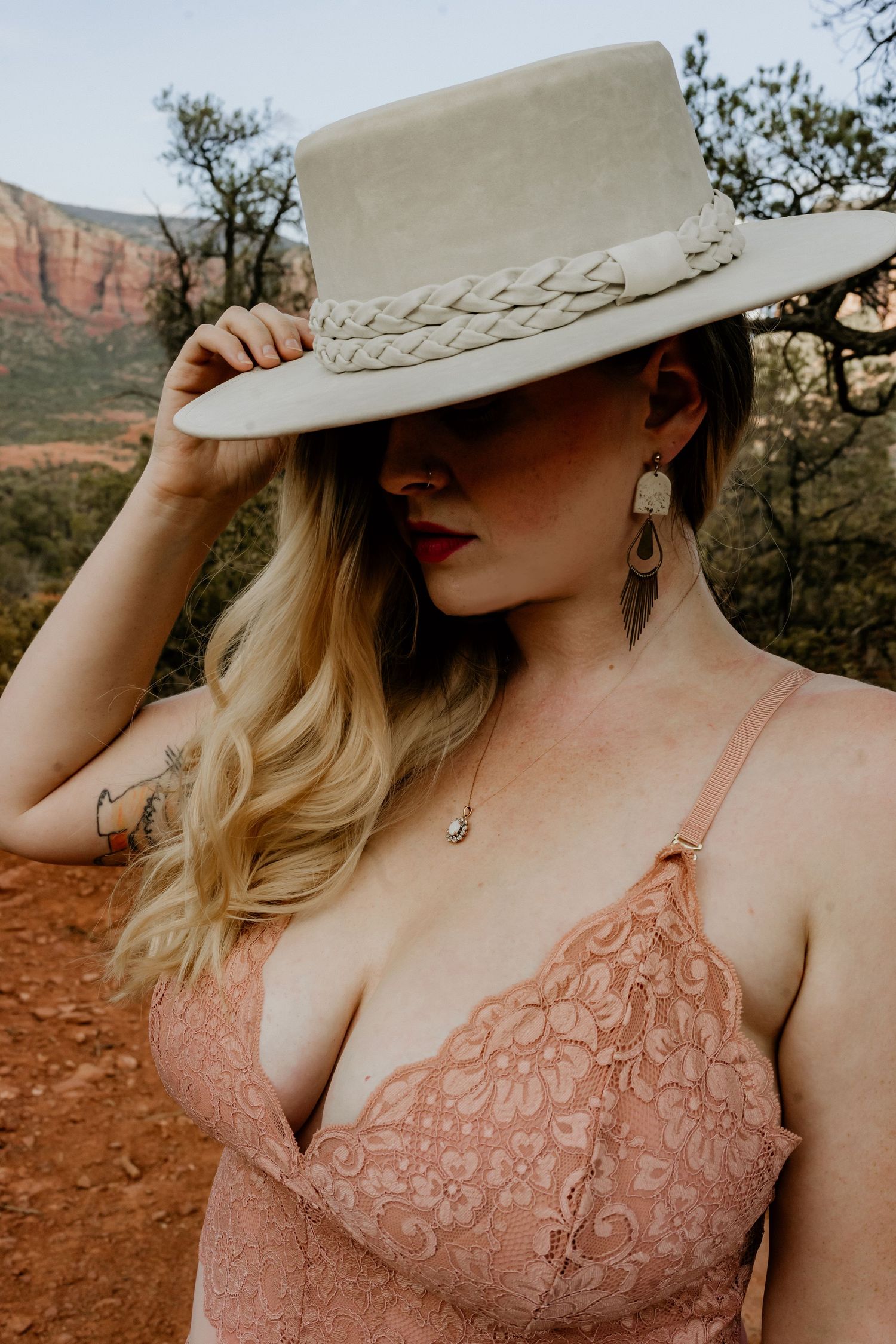 Western style portrait with beige hat and lace top against red rock cliffs.