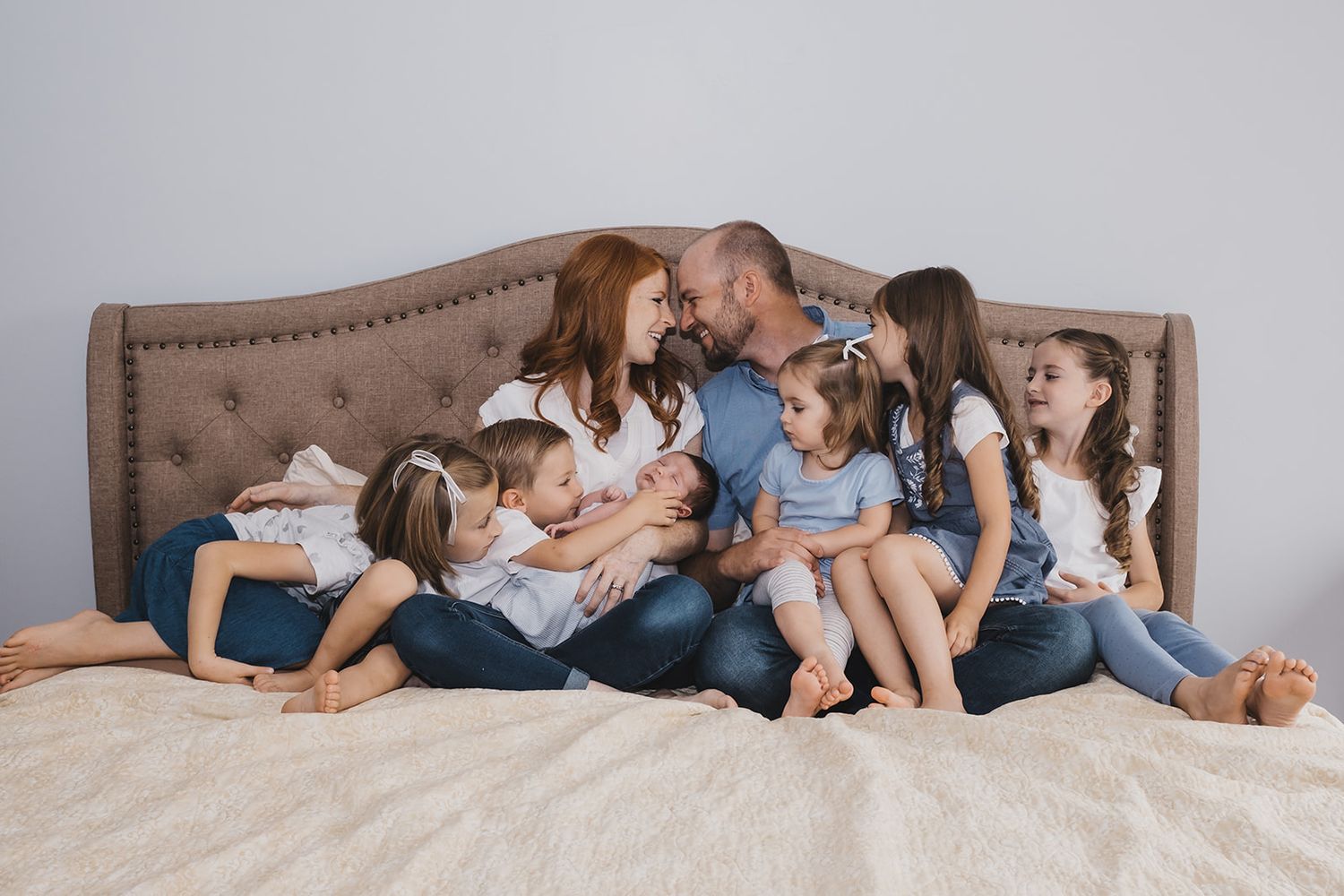 A Family with newborn baby at home in Layton, Utah sitting on their bed together.