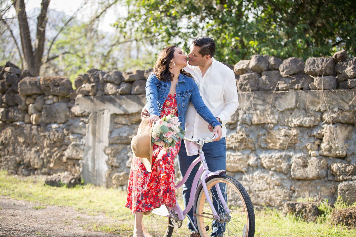 Family with bicycle poses against rustic stone wall on spring day.