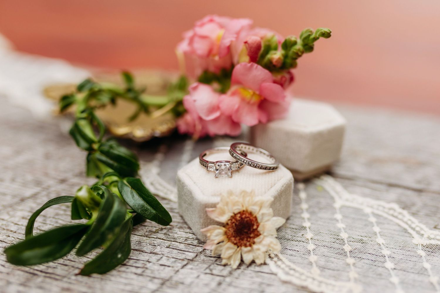 Wedding rings rest on a hexagonal white ring box surrounded by pink snapdragons and delicate flowers.