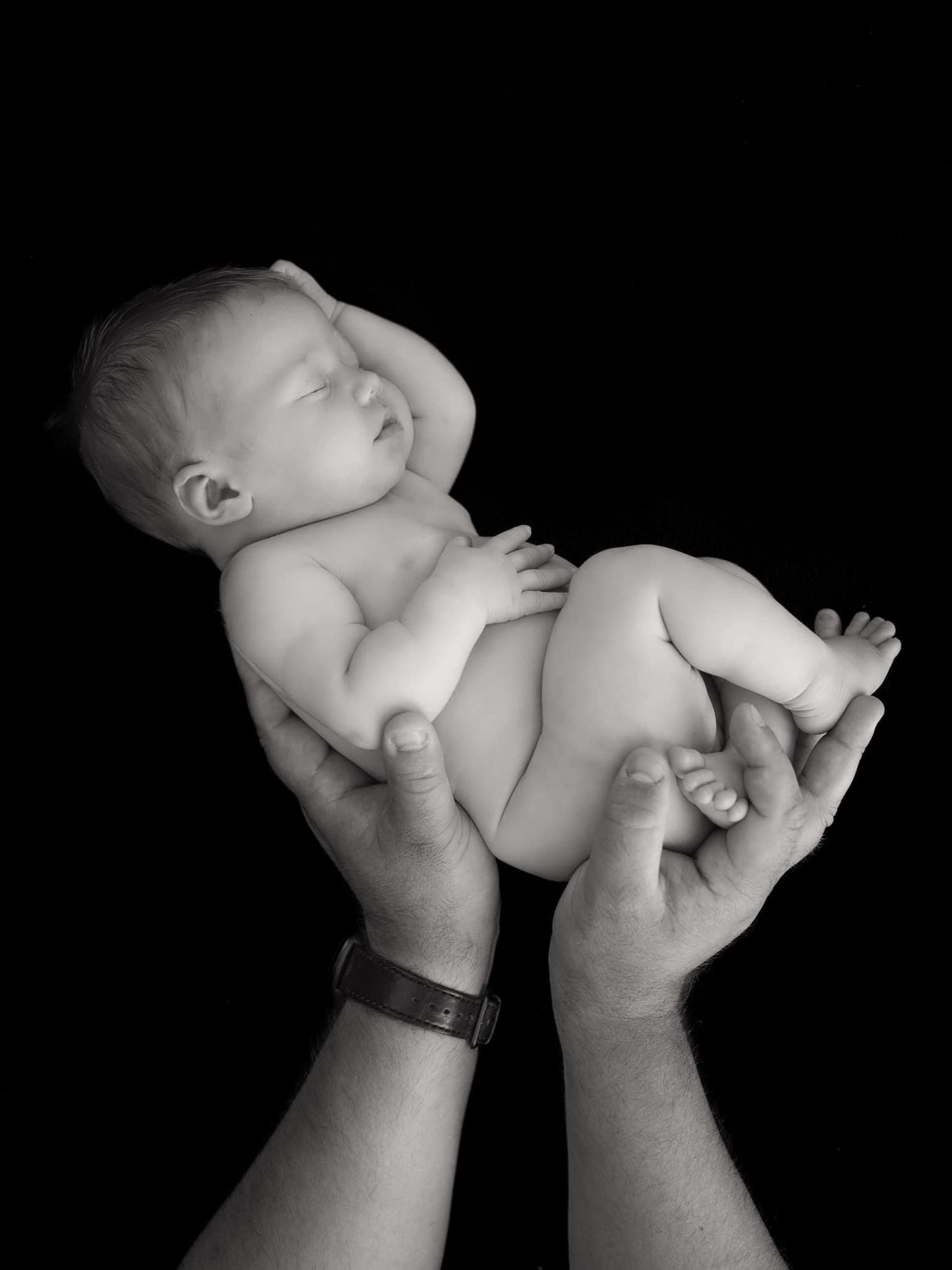 Black and white artistic photo of baby feet against dark background.