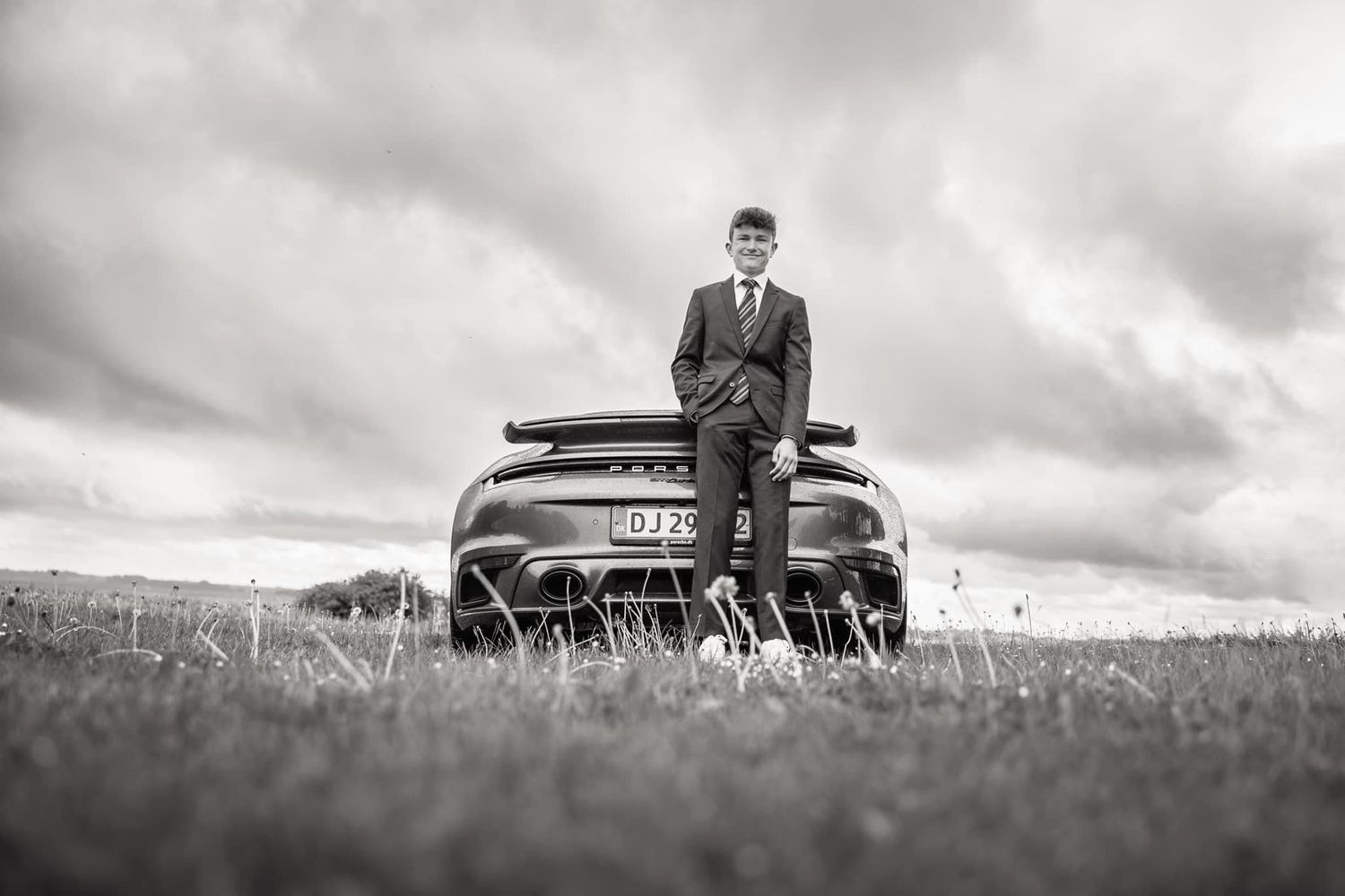 Panoramic black and white photo of person with vintage car in grassy field.