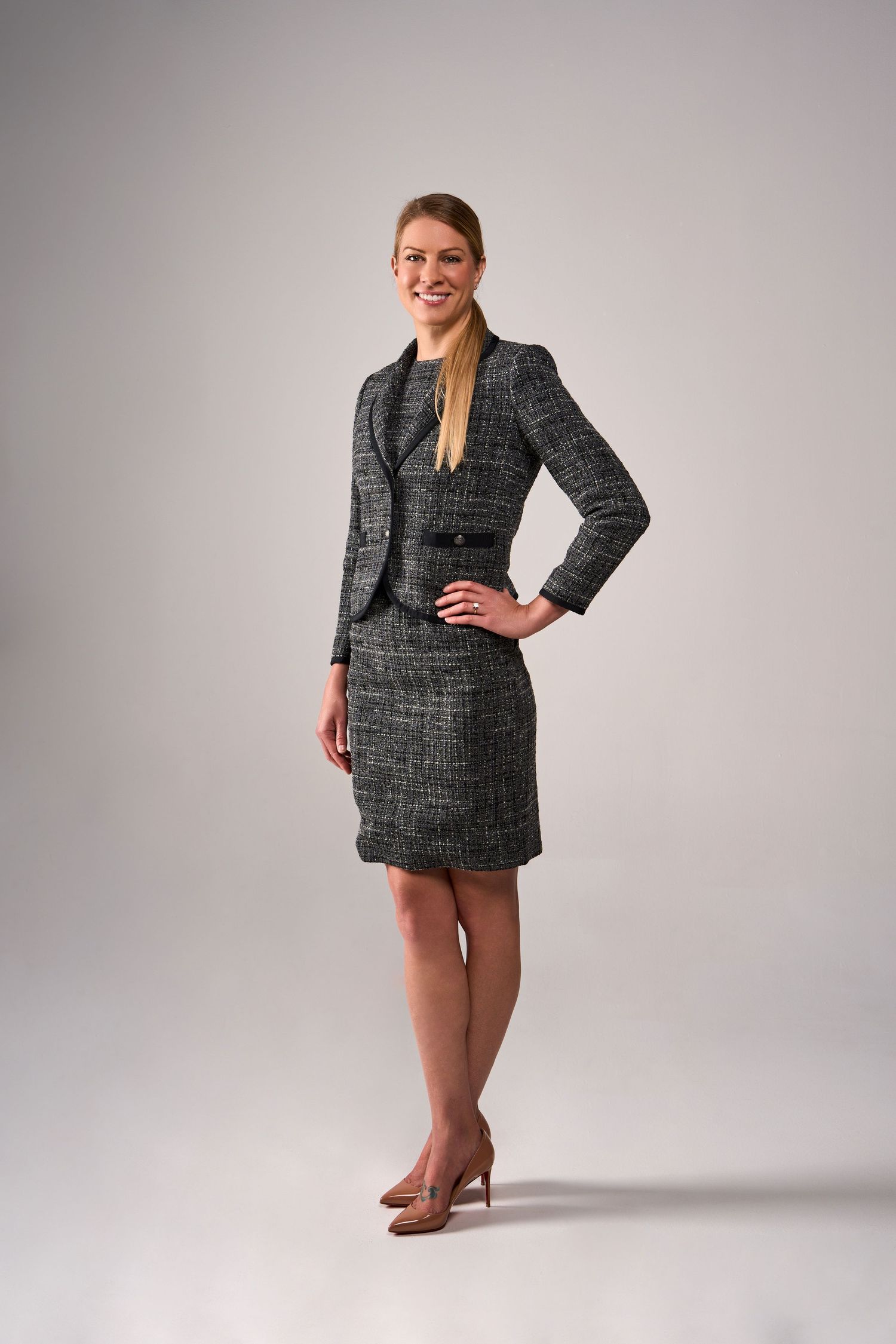 Professional woman in gray tweed suit dress poses confidently against neutral backdrop.