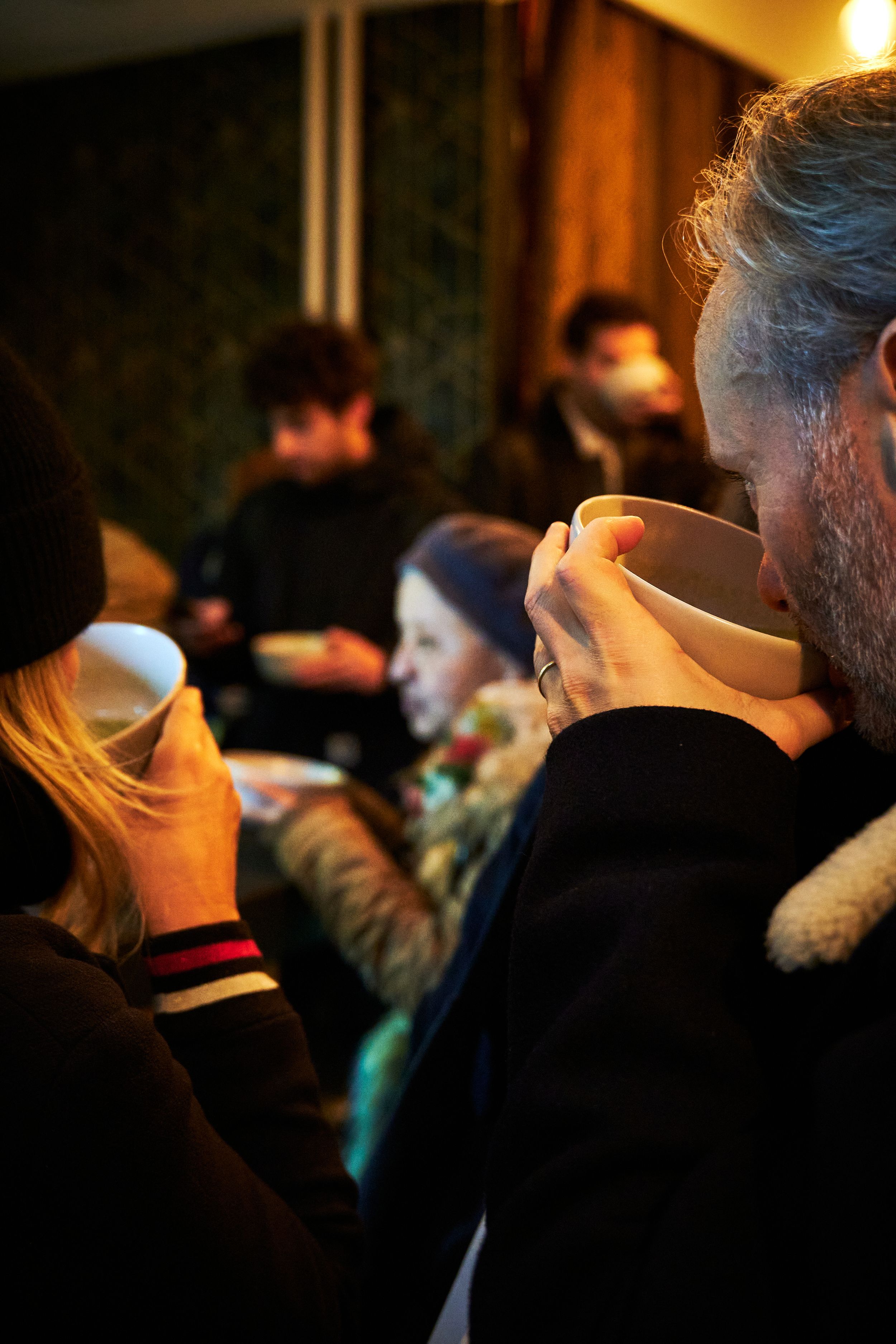 People holding white soup bowls in a crowded, dimly lit space.