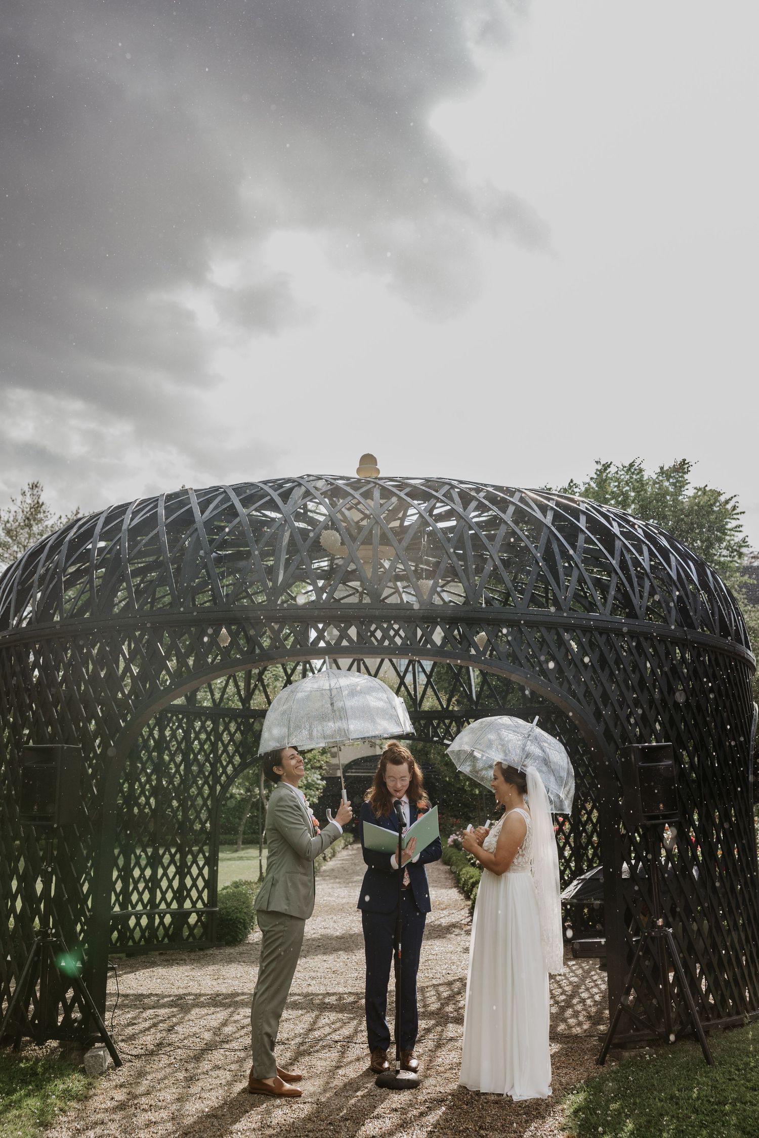 Couple exchanging vows under modern gazebo in rain with clear umbrellas, outdoor wedding. New Bedford, Ma Miranda Photo & Co
