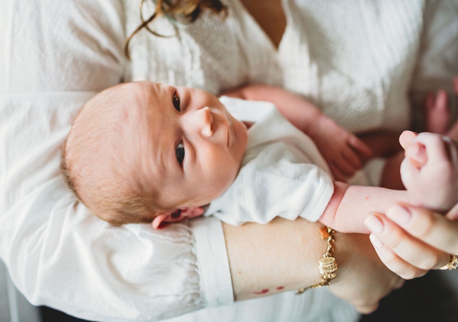 Baby wearing a white onesie lies in someone's lap while smiling at the camera.