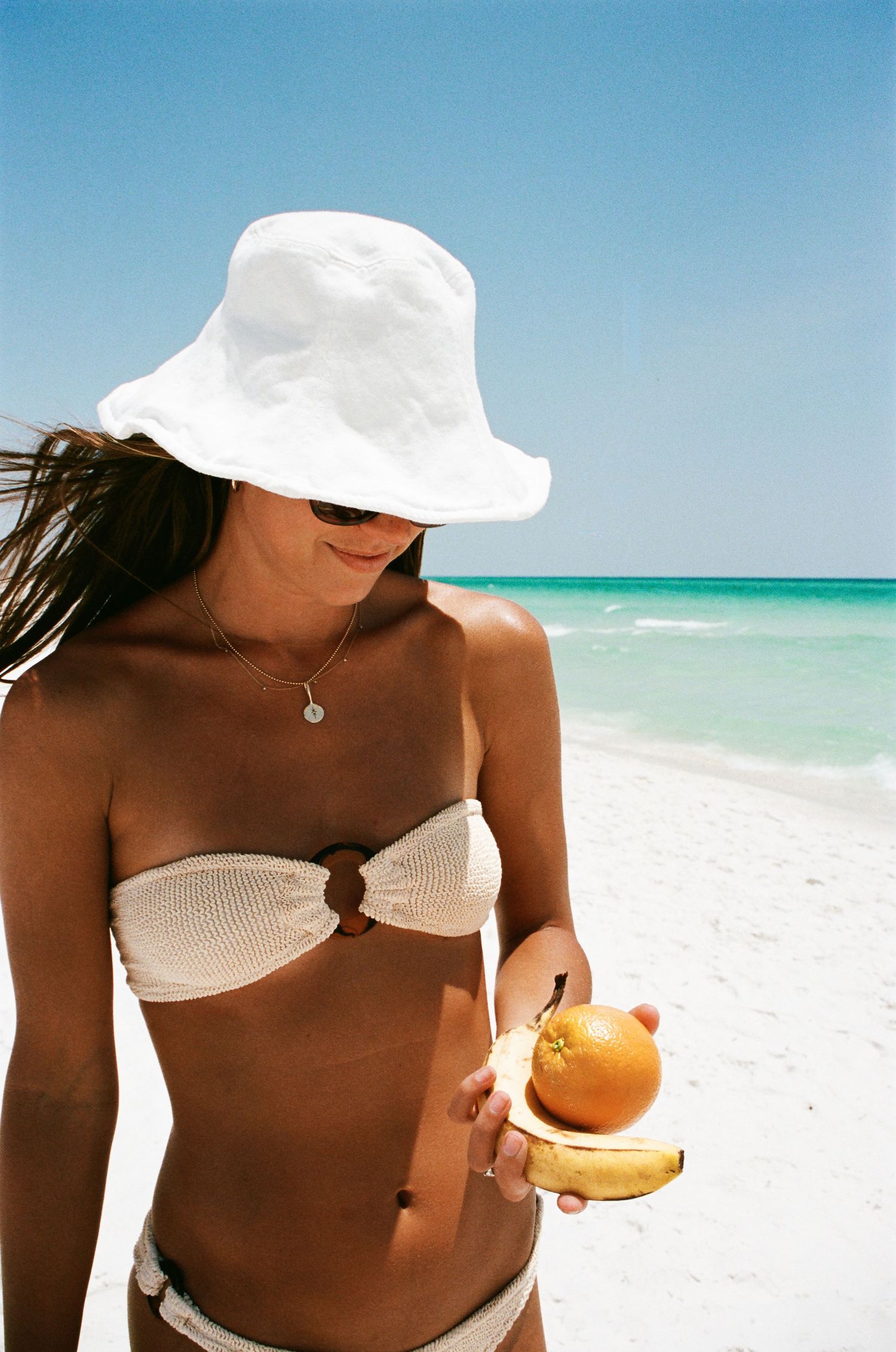 Person wearing white hat enjoying coconut drink on tropical beach.